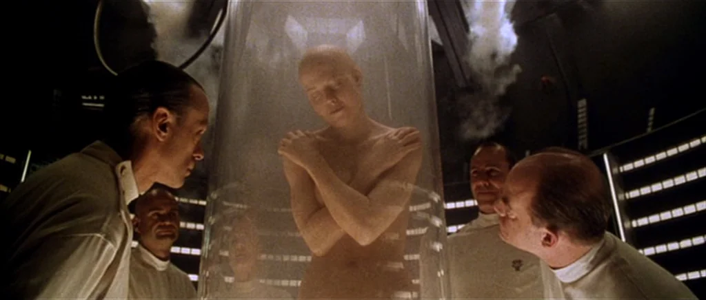 Alien: Resurrection (1997) movie still: medium — A stark white laboratory features a large cylindrical glass chamber emitting faint vapor. Several…