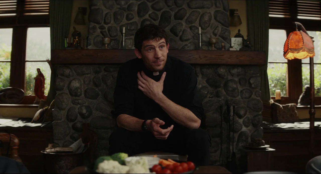 Wake Up Dead Man (2025) movie still: medium — A rustic interior features a fieldstone fireplace as a backdrop to a seating area. A man dressed as a…