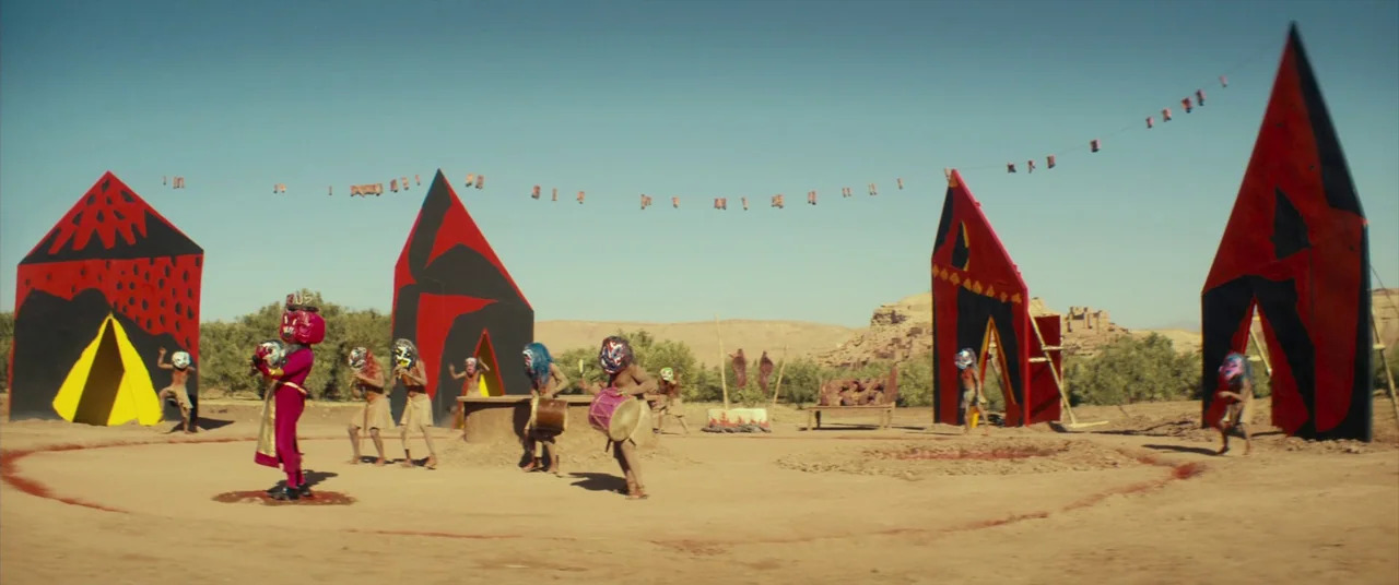 Seneca: On The Creation Of Earthquakes (2023) movie still: wide — A desert area features geometric, brightly painted red and black tribal…