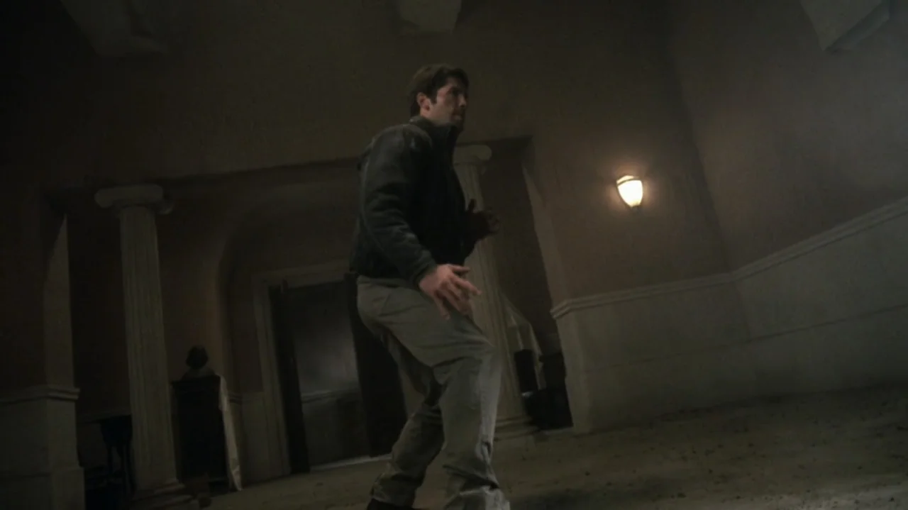The Shepherd (2023) movie still: fullbody — A dim lobby with architectural columns and a dark floor features a lone figure. A man in tactical attire…