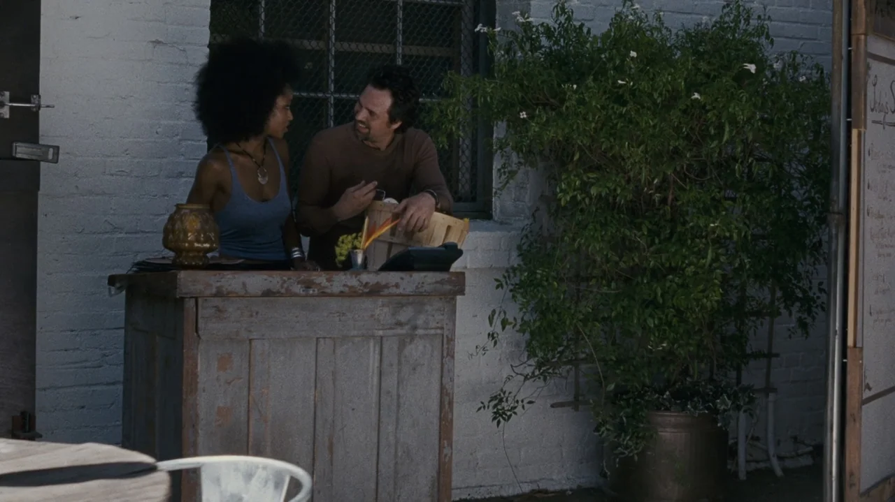 The Kids Are All Right (2010) movie still: medium — An outdoor market stall made of worn wood sits against a painted brick wall. A man and woman…