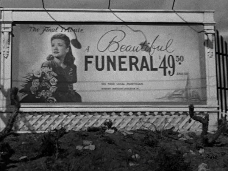 Saboteur (1942) movie still: wide — A large outdoor billboard stands against a backdrop of dark, barren landscape. The printed advertisement…