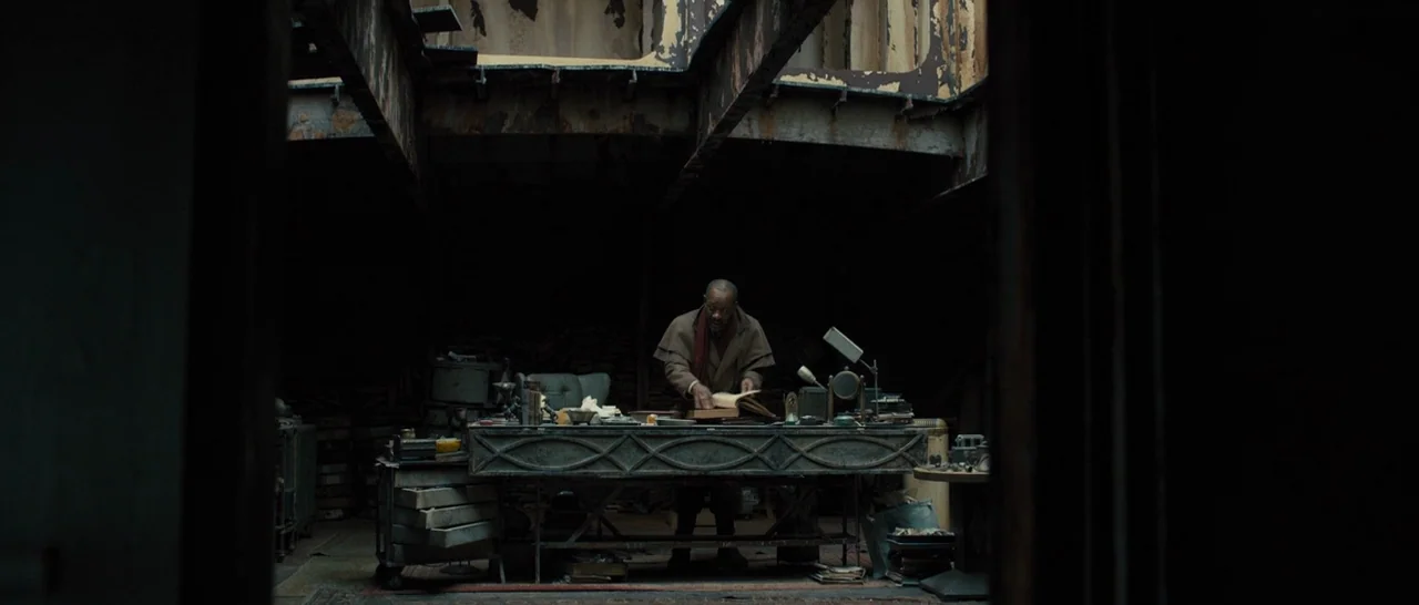 Blade Runner 2049 (2017) movie still: wide — A cluttered, dark interior with exposed industrial structural beams and rusted metal elements. An…