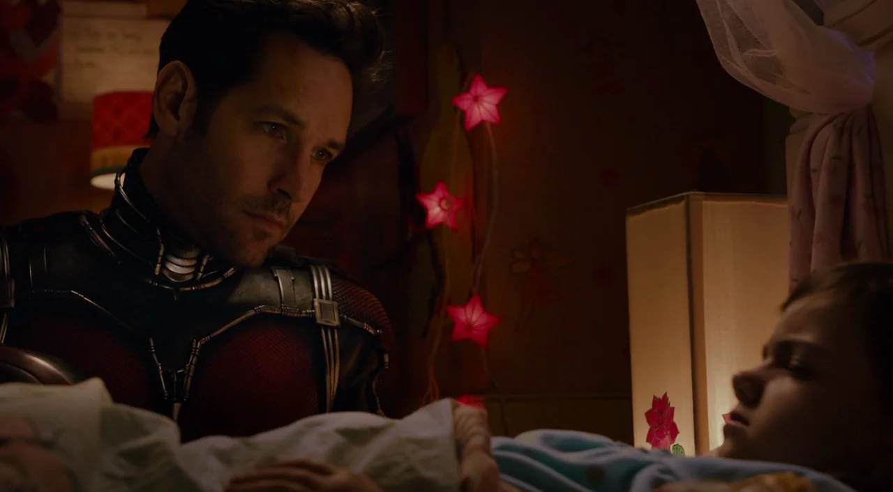 Ant-Man (2015) movie still: medium — A dimly lit room with star-shaped string lights hanging on a decorated wall. A man in a high-tech suit watches…