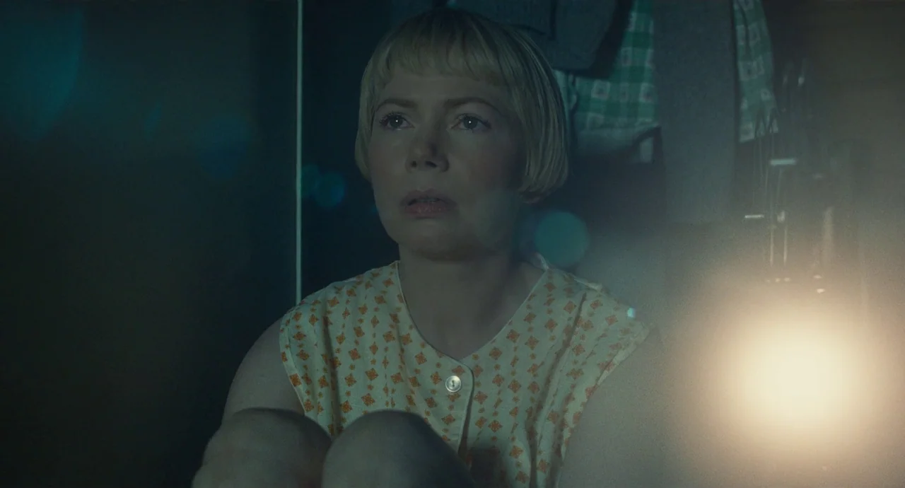 The Fabelmans (2022) movie still: medium — A dimly lit indoor space features a woman in a patterned sleeveless top. She sits alone while staring…