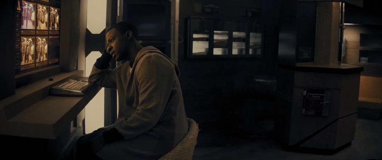 Domain (2017) movie still: medium — A dark monitoring station features a wall-mounted screen displaying multiple camera feeds. A man sits at a desk…