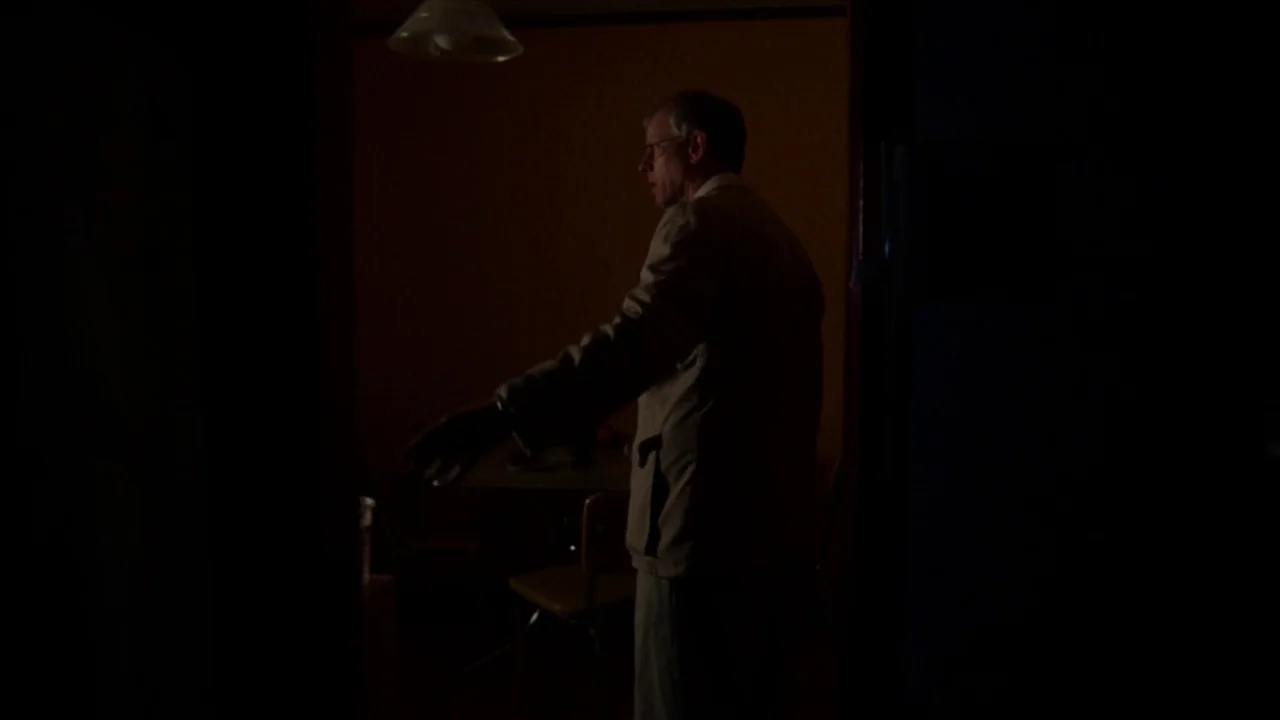 A Horrible Way To Die (2010) movie still: medium — A dark dining room with a solitary pendant light glowing in the background. An elderly man in a…