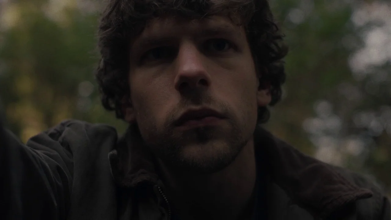 Night Moves (2013) movie still: closeup — A man's face fills the frame against a backdrop of blurred forest greenery. He gazes downward directly…