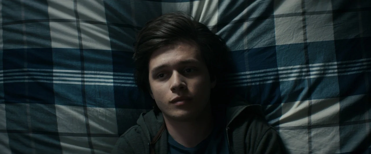 Strange but True (2019) movie still: closeup — A close overhead shot of a young man lying on a plaid bedsheet pattern. The subject rests against the…