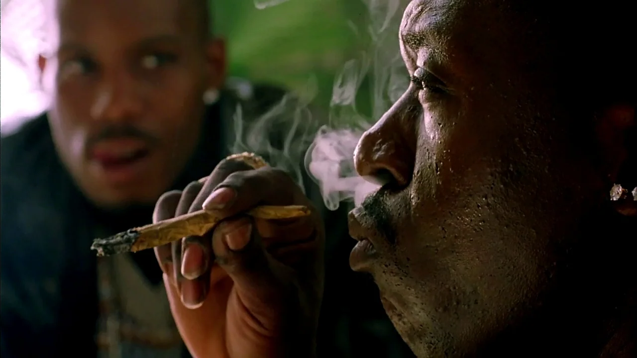 Belly (1998) movie still: closeup — A dark indoor space is filled with wisps of smoke between two individuals. A man with a goatee observes as…