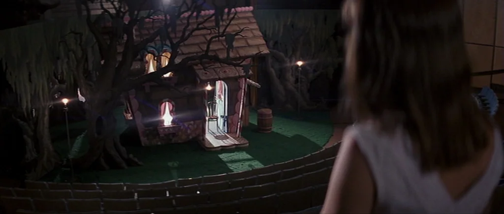Cape Fear (1991) movie still: medium — A woman stands in the dark auditorium looking down at a small constructed stage set. The set features a…