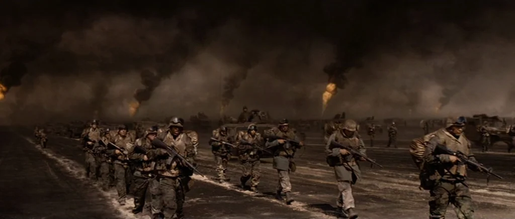 Jarhead movie still: wide — A desolate landscape is covered in thick, dark smoke from burning oil well fires. Soldiers in tactical gear move in…