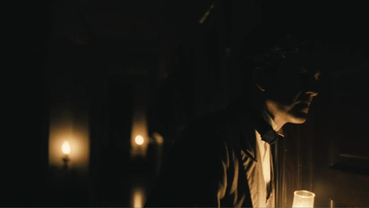 Demon in the White House (2021) movie still: medium — A dark indoor corridor features two distant lamps casting light on the wall surfaces. A man in…
