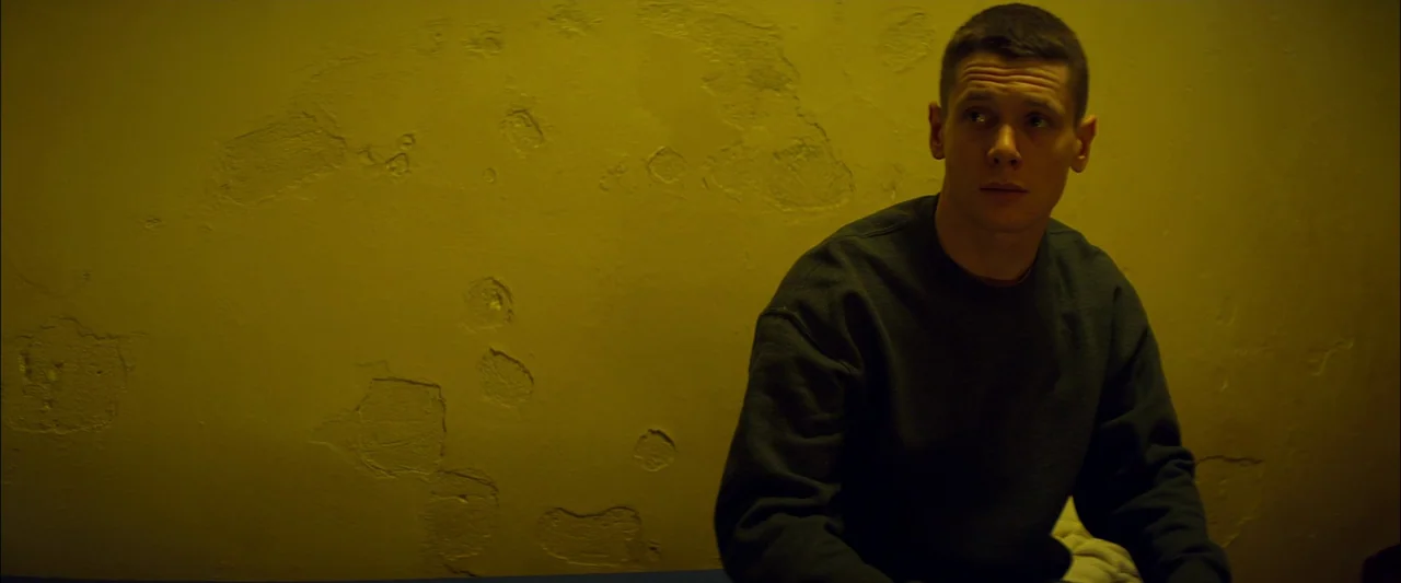 Starred Up (2013) movie still: medium — A bare room features a yellow painted wall with significant patches of peeling plaster. A young man with…