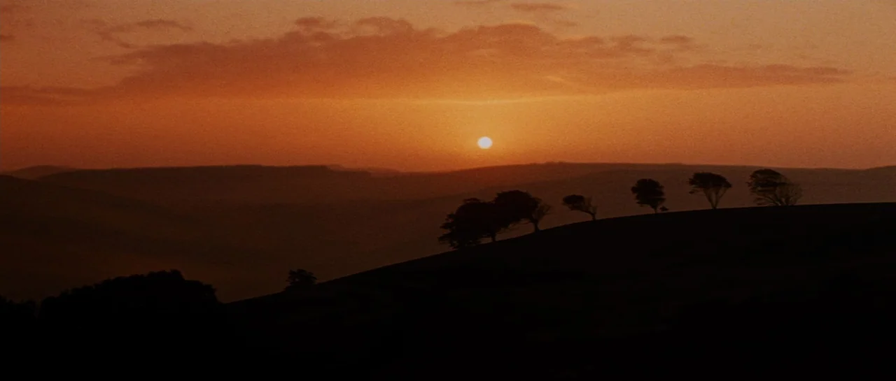 Macbeth (1971) movie still: establishing — A landscape of rolling hills silhouettes against a glowing orange sunset sky. Several scattered trees…
