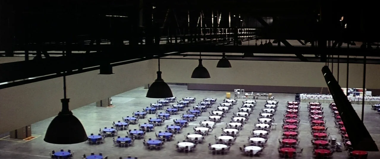 The Parallax View (1974) movie still: establishing — A vast, industrial-style banquet hall features high ceilings and exposed support structures.…