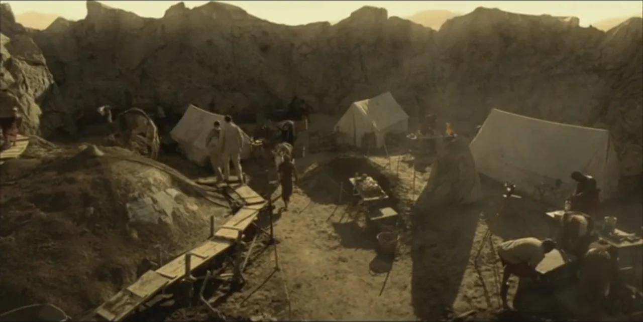Exorcist: The Beginning (2004) movie still: wide — A dusty excavation camp sits at the bottom of a steep rocky canyon. Several white canvas tents…