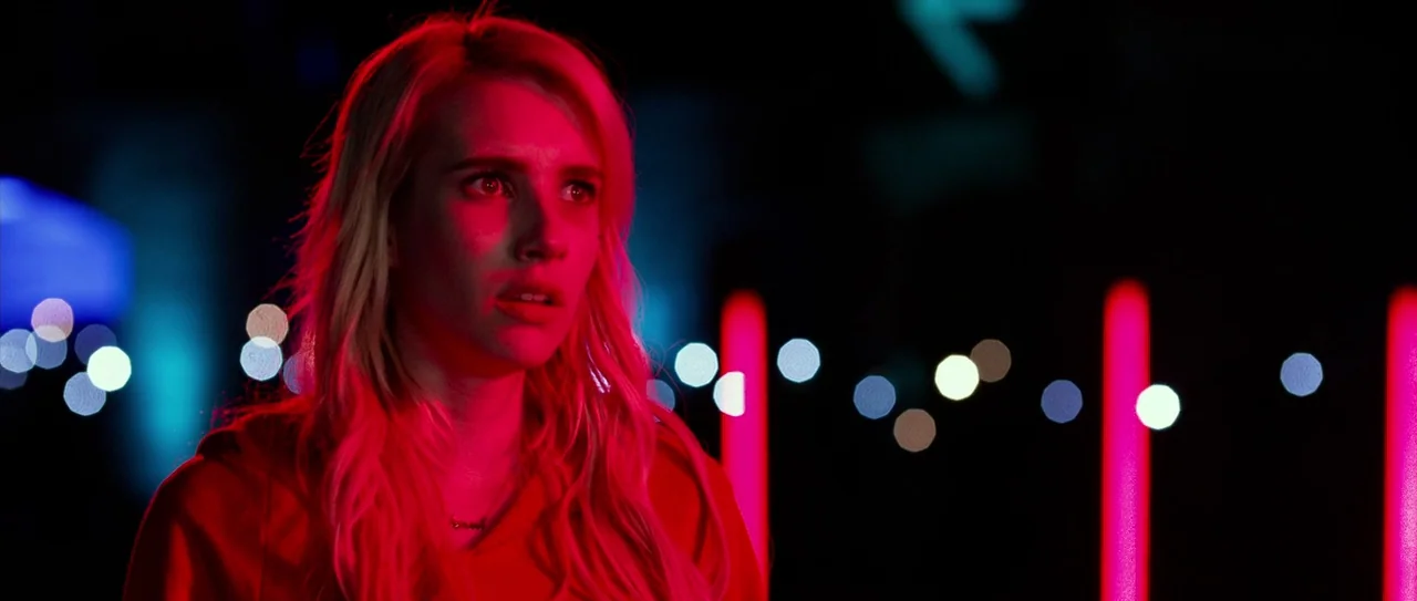 Nerve (2016) movie still: closeup — A dark outdoor setting at night features vibrant red vertical neon light strips. A young woman with blonde hair…