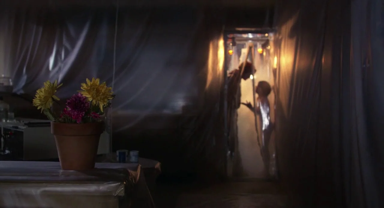 E.T. The Extra-Terrestrial (1982) movie still: wide — A dark, plastic-draped enclosure is lit from within by a singular warm light source. A man and…