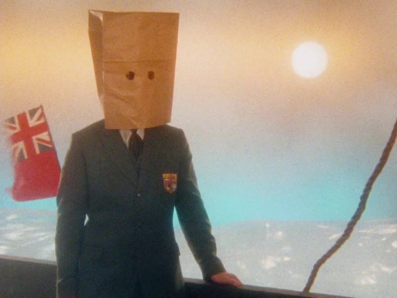 The Twentieth Century (2019) movie still: medium — A person with a paper bag over their head stands on a ship deck. A bright sun hangs in a hazy sky…
