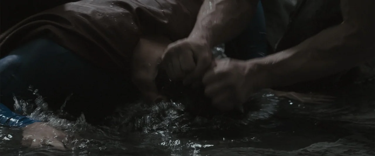 Superman Returns (2006) movie still: closeup — A dark shallow body of water at night with splashing liquid surfaces. Two figures are submerged and…