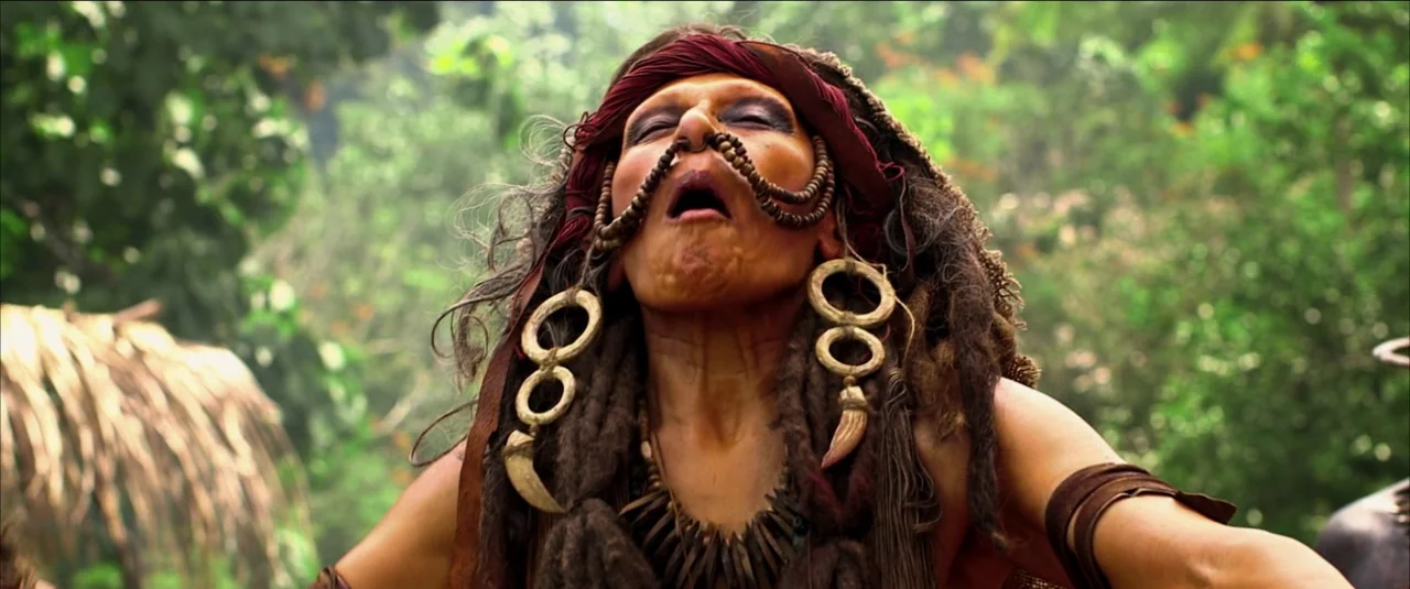 Green Inferno (2013) movie still: closeup — A dense green jungle setting with blurred foliage background and primitive adornments. A woman with…