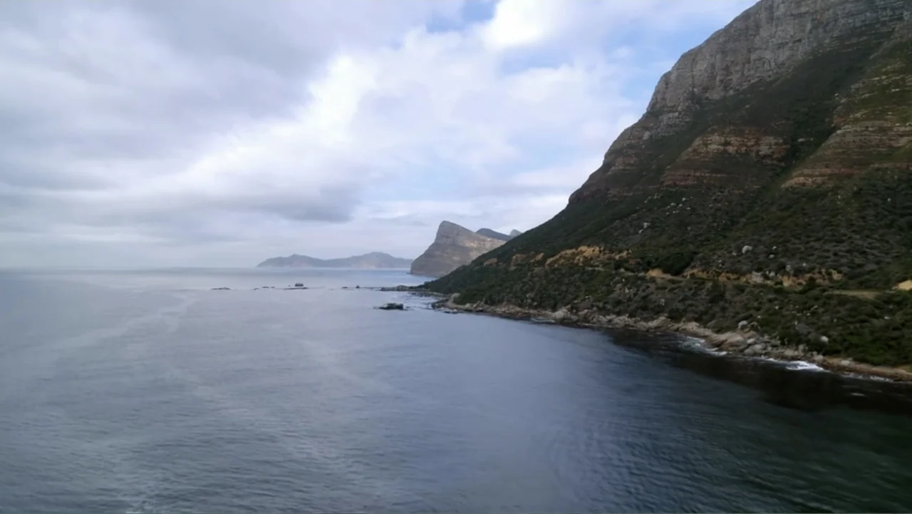 Alien Sharks: Strange New Worlds (2023) movie still: establishing — A vast coastal landscape features steep mountains meeting a dark, calm ocean.…