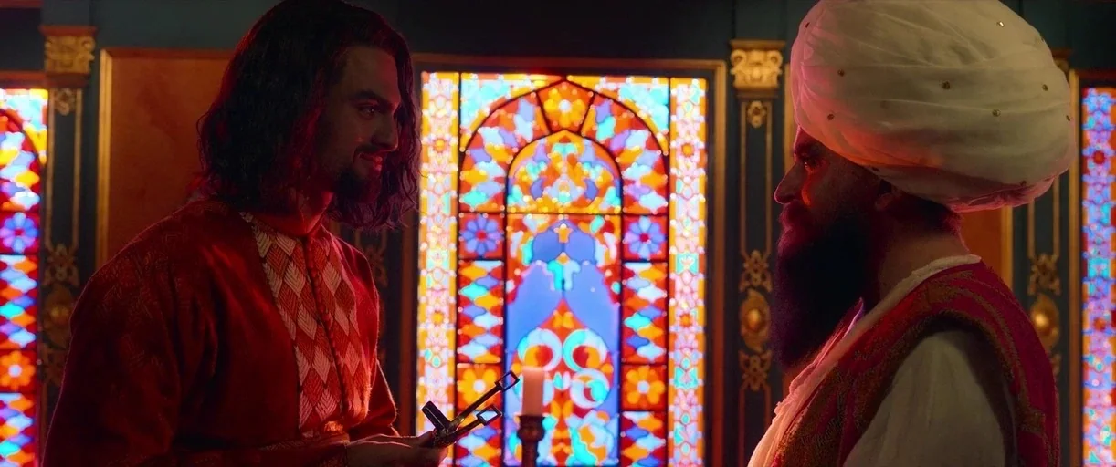 Three Thousand Years of Longing (2022) movie still: medium — A dimly lit room features walls decorated with vertical stained glass panels. Two men…