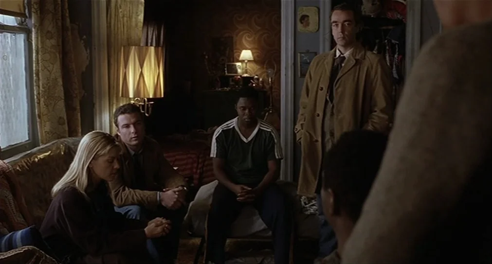 The Hurricane (1999) movie still: medium — An aged apartment room has floral patterned wallpaper and a cluttered, dated aesthetic. Four people are…