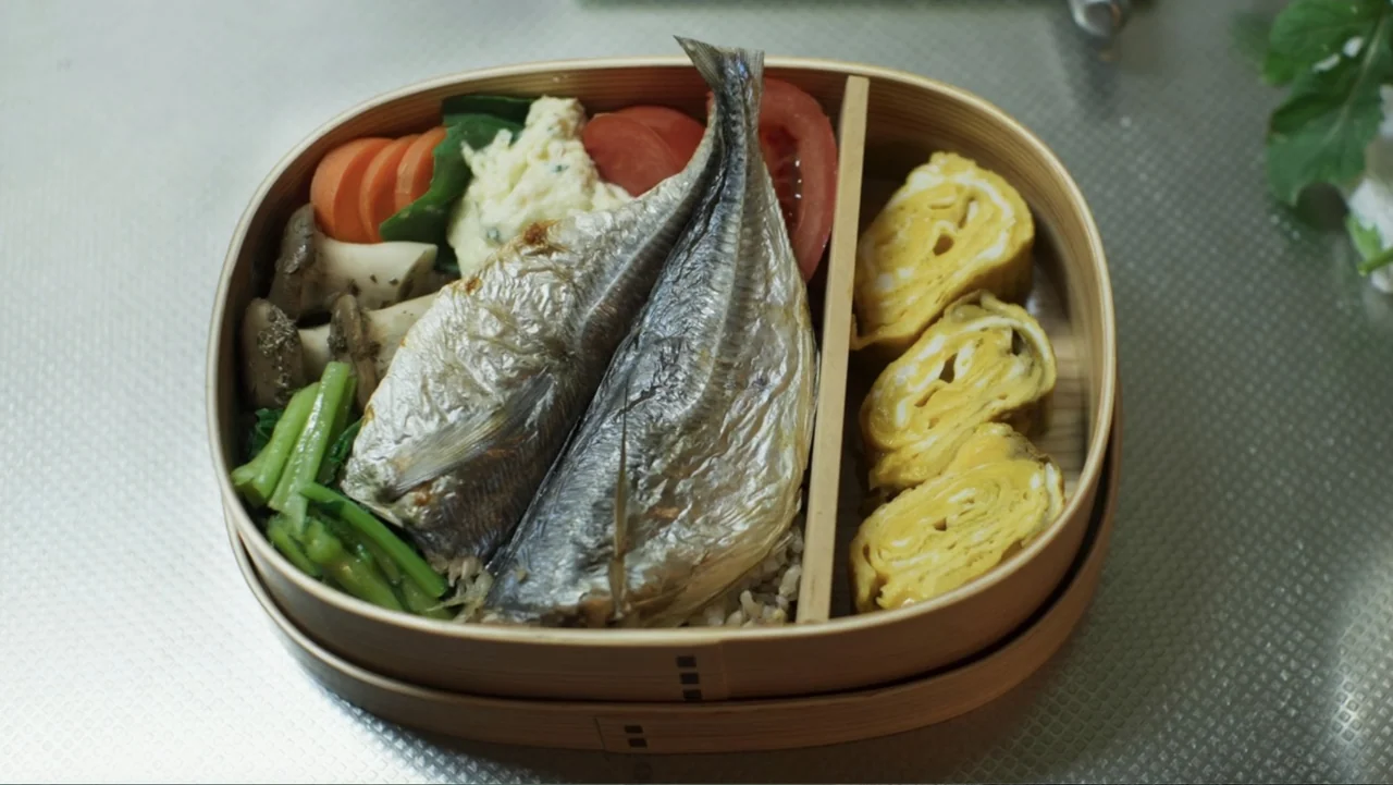 Victoria's Secret: The Tour '23 (2023) movie still: closeup — A wooden bento box sits on a silver-toned textured surface. The meal contains grilled…