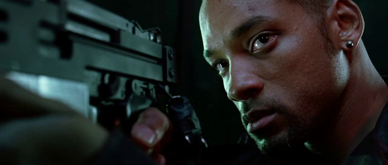 I, Robot (2004) movie still: closeup — A dark, enclosed space with heavy shadows obscuring the surroundings. A man grips a firearm while looking…
