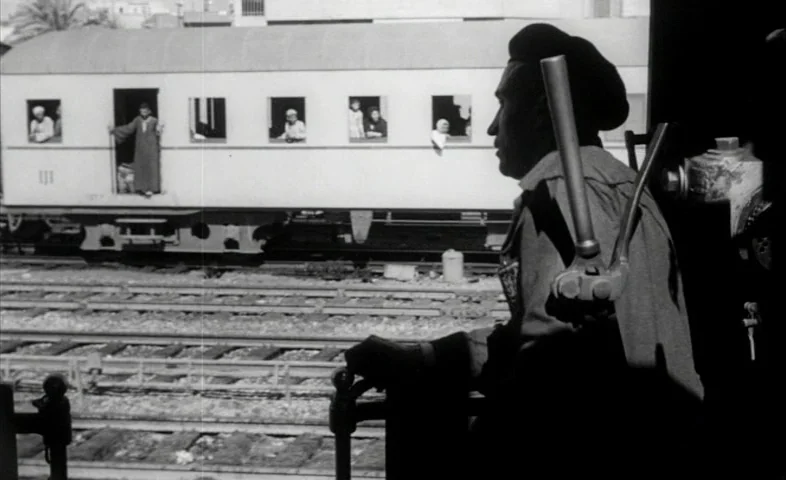 Cairo Station (1958) movie still: medium — A train conductor looks from the cockpit toward a passenger carriage on adjacent rails. Several…