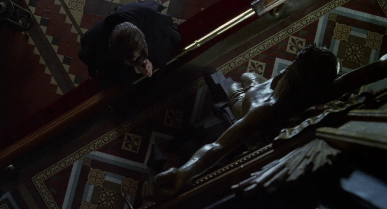 Amistad (1997) movie still: wide — A top-down view of an ornate, tiled church floor featuring a dark kneeling man. A large wooden crucifix lies…