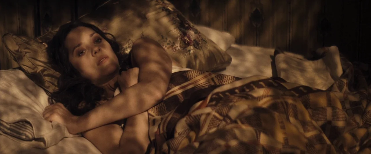 The Immigrant (2013) movie still: medium — A woman rests in a bed covered by a thick, checkered blanket. Patterns of light filter across her body…
