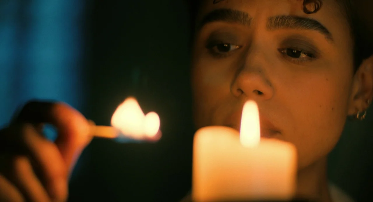 The Killer (2024) (2024) movie still: closeup — A close-up view shows a person in a dim setting lit by firelight. A woman holds a lit match to a…