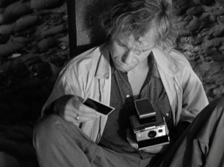 Alice in the Cities (1974) movie still: medium — A man sits on the floor of a dark, rocky bunker environment. He examines a small photograph while…