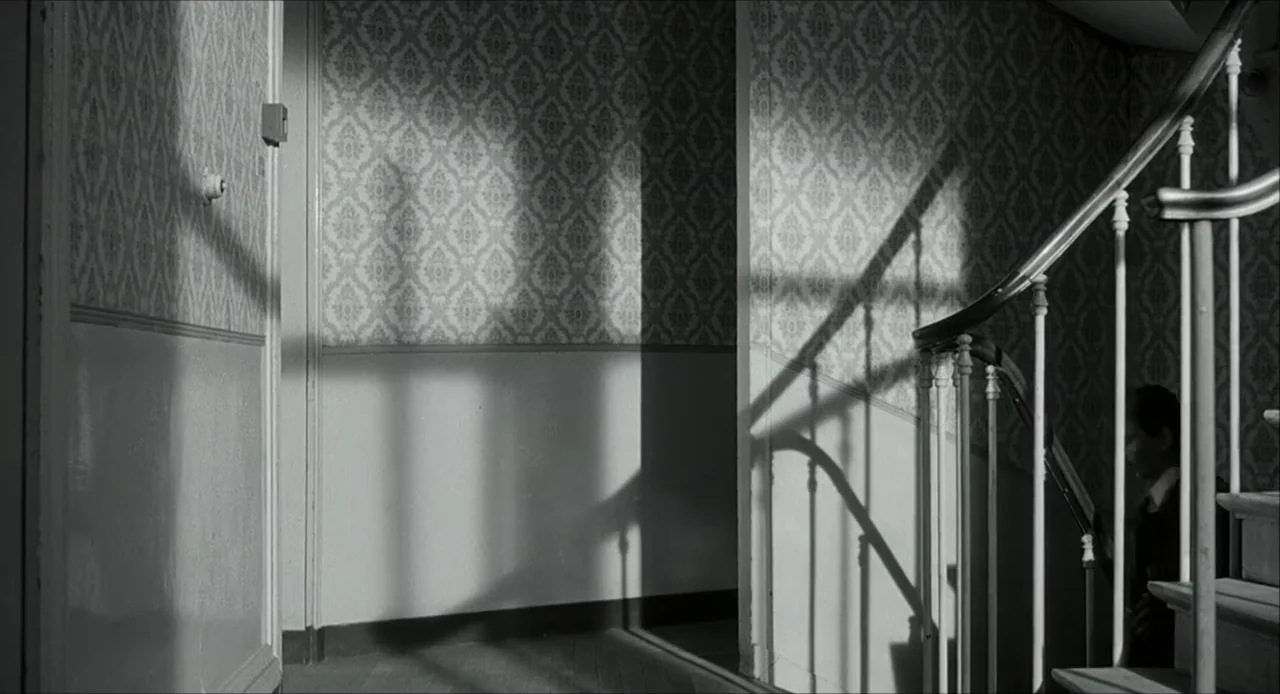 The Bohemian Life (1945) movie still: wide — A residential interior features patterned floral wallpaper and a wooden staircase with iron railing. A…