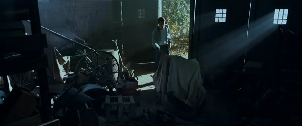 The Curious Case Of Benjamin Button (2008) movie still: wide — A dark, cluttered shed contains various tools, wheels, and machinery beneath dusty,…