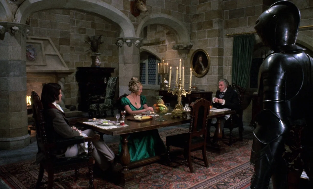 The Horror of Frankenstein (1970) movie still: wide — A stone-walled room with vaulted ceilings contains a long dining table set with fruit. Three…