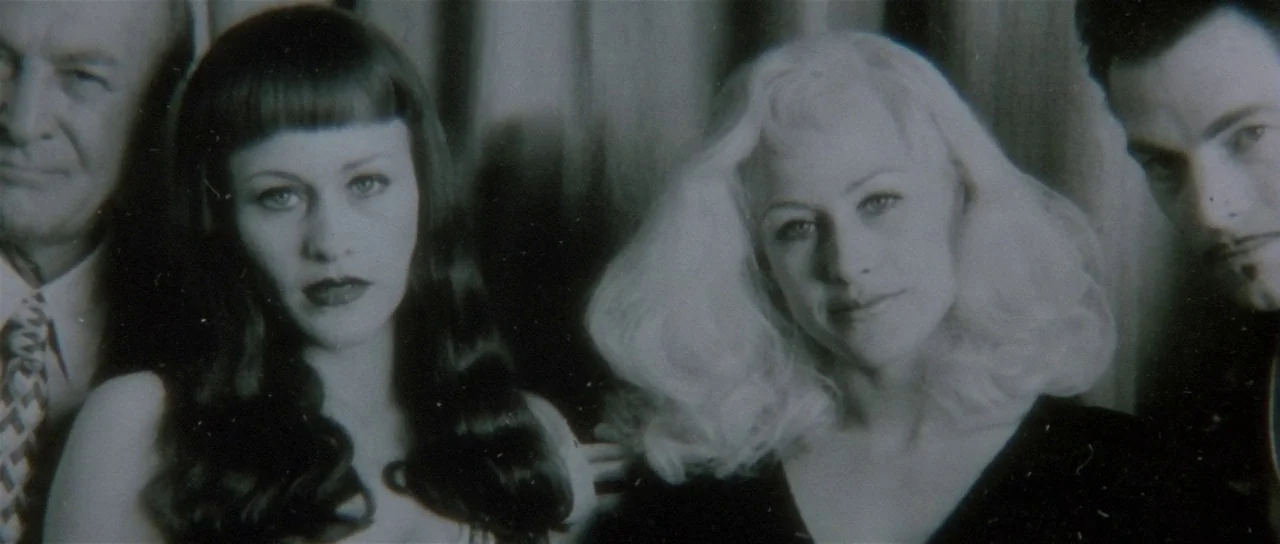 Lost Highway (1997) movie still: medium — Four people stand in a line before a heavy, dark, pleated curtain backdrop. The group consists of two men…