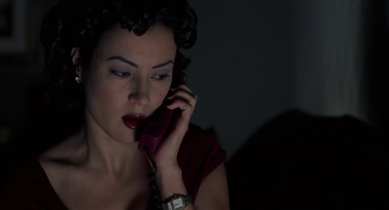 Bound (1996) movie still: closeup — A woman sits in a dimly lit, dark environment while talking on the phone. She holds the telephone handset to her…
