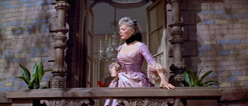 Gigi (1958) movie still: medium — An elegant exterior stone balcony features ornate carved pillars flanking an open doorway. A blonde woman wearing…