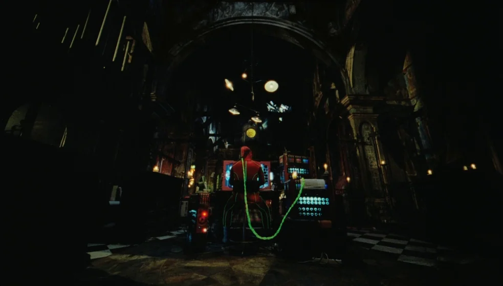 The Zero Theorem (2013) movie still: wide — A dark, arched stone interior resembling a cathedral with a black and white checkerboard floor. A…