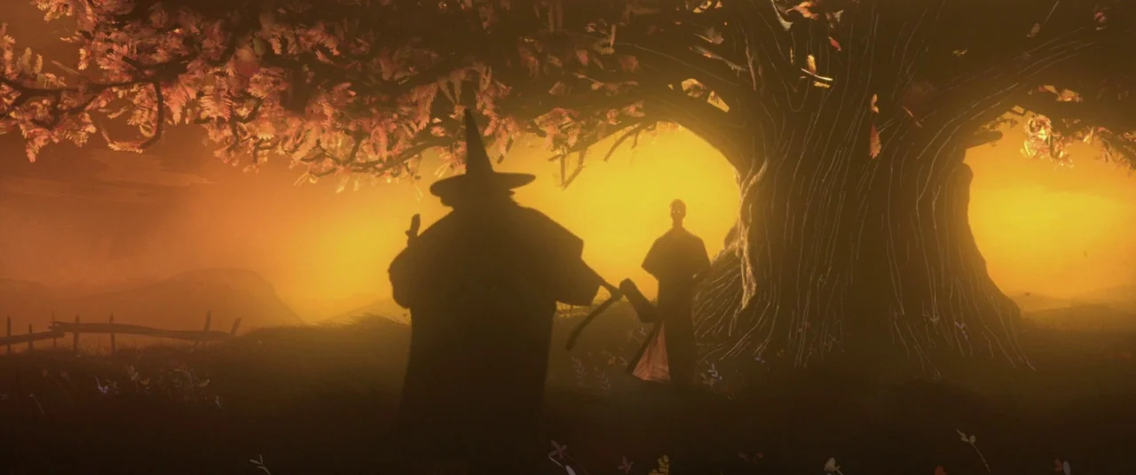 A Monster Calls (2016) movie still: wide — A field at dusk features a large gnarled tree with glowing autumn foliage. A cloaked figure with a staff…
