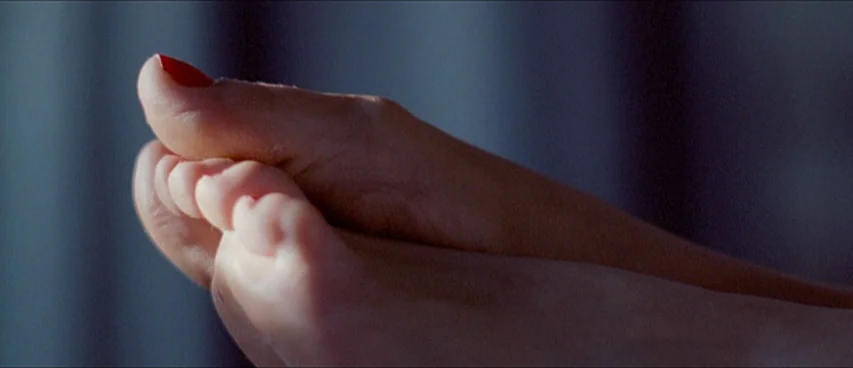 This Movie Is Broken (2010) movie still: closeup — A pair of human feet rest against a dark background in a dim space. The big toe is painted with…