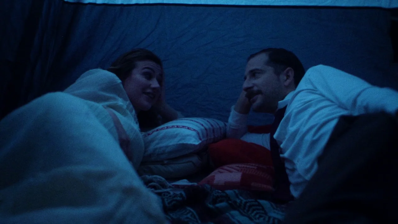 Strawberry Mansion (2021) movie still: medium — A man and woman lie inside a dark fabric enclosure lit with blue tones. They are lying on blankets…