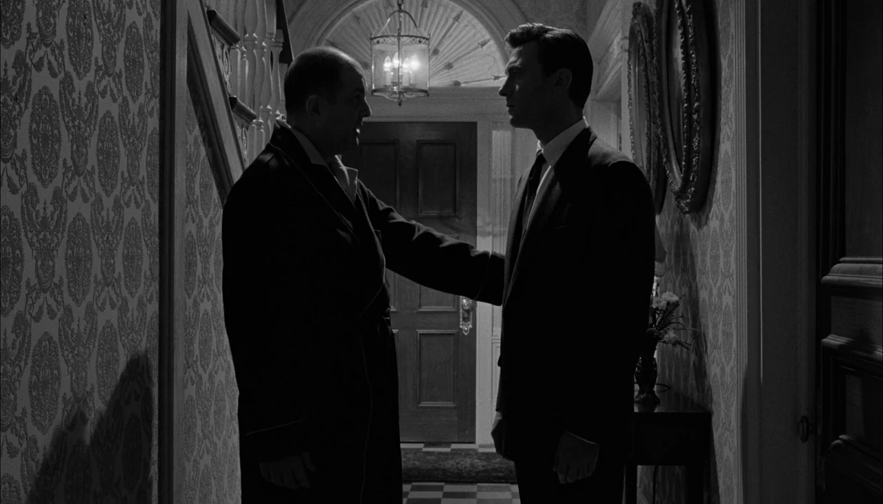 The Manchurian Candidate (1962) movie still: medium — A narrow residential hallway with patterned wallpaper and a distant doorway under a light. An…