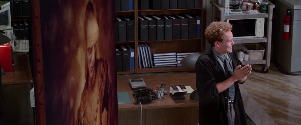 Ghostbusters 2 (1989) movie still: medium — An office interior features wooden shelving units filled with black binders and a desk. A young man…