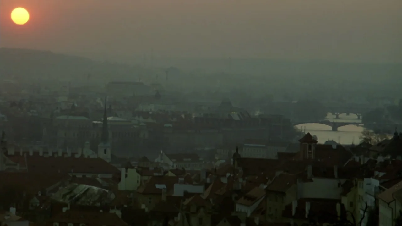 6 Bullets (2012) movie still: establishing — A panoramic view of a European city featuring dense red-tiled roofs and distant bridges. The sun…