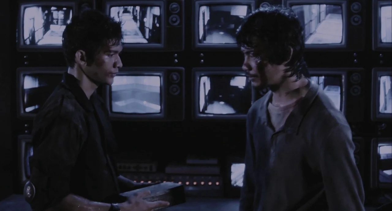 The Raid (2012) movie still: medium — A dark room lined with multiple glowing CRT monitors showing static security footage. Two men stand facing…